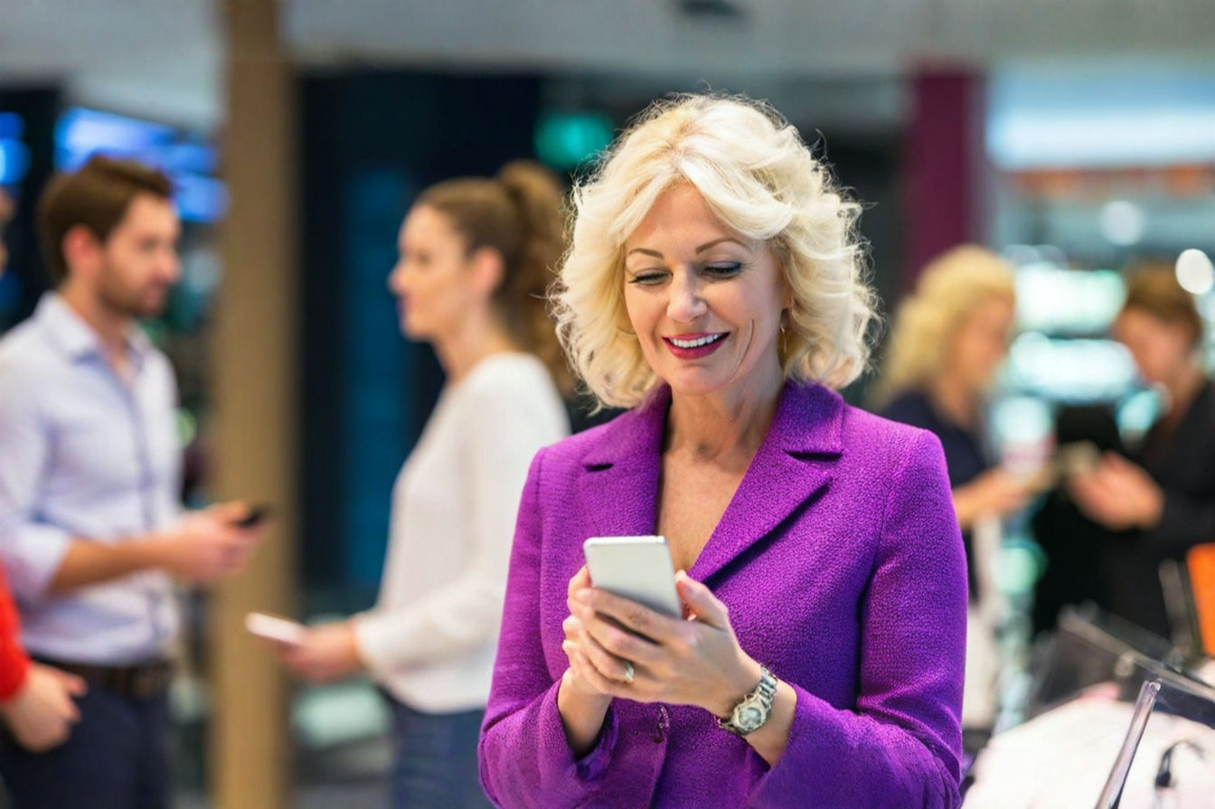Professional, brightly lit photograph showing a group of people of various ages holding and interacting with different models of modern smartphones. The background is a clean, slightly blurred retail store or tech convention setting, suggesting the act of choosing or comparing devices. The image should convey a sense of informed decision-making and the variety of options available.