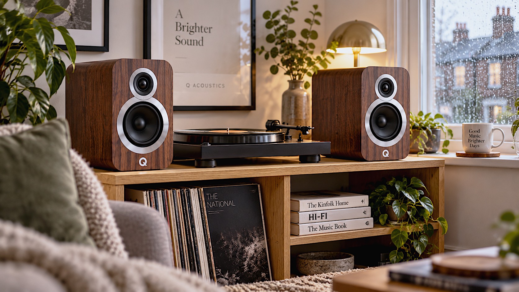 photograph of a pair of English Walnut Q Acoustics 3010i speakers sitting on a stylish, minimalist oak bookshelf in a cosy British living room. A vinyl record player sits nearby, and soft, warm light filters through a rainy window.