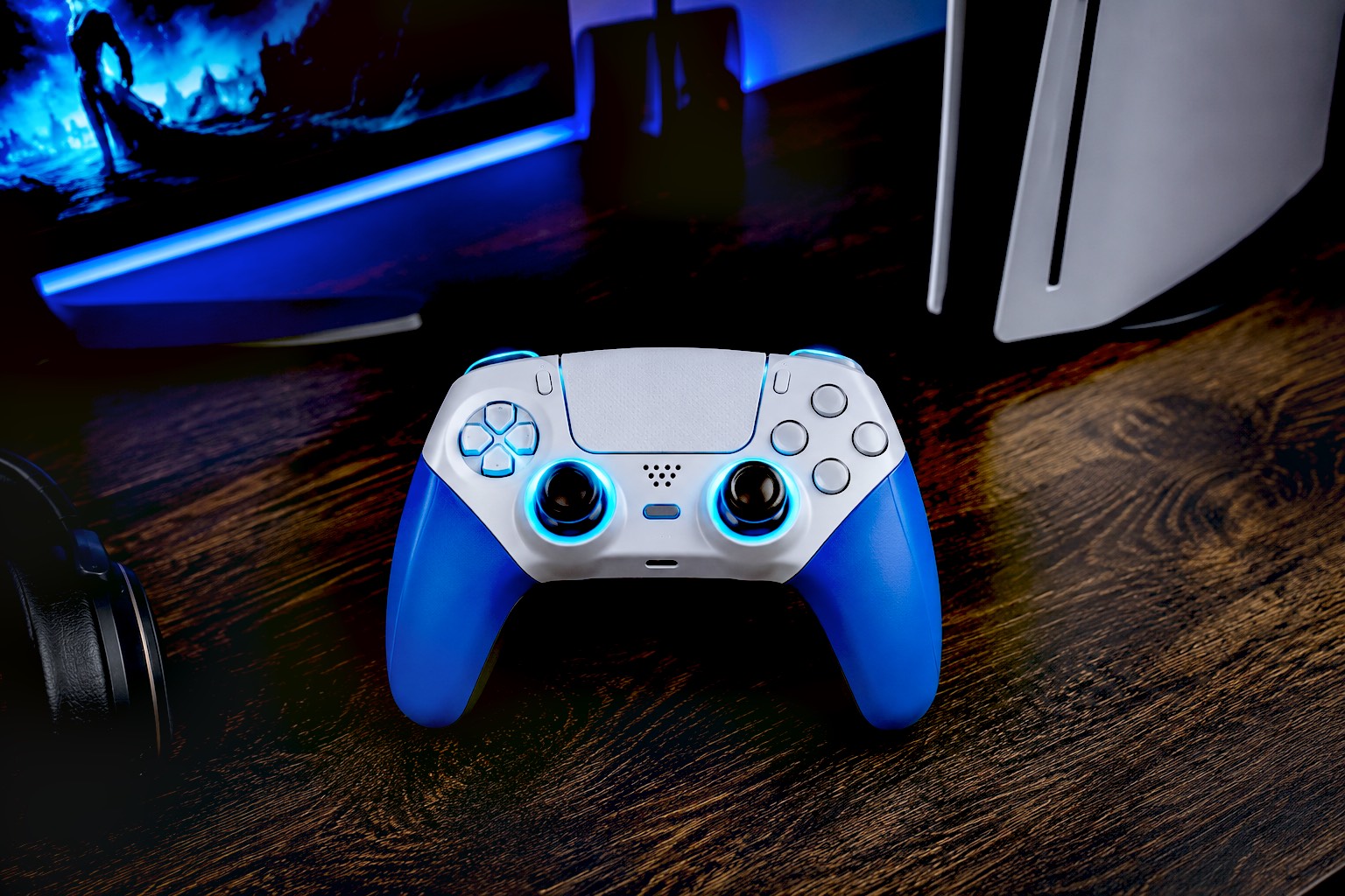 A hyper-realistic, top-down photograph of the blue and white SFGSUP wireless controller resting on a dark wooden gaming desk. The controller's RGB rings are glowing a subtle cyan. In the softly blurred background, a glowing PC monitor and a sleek white PS5 console are visible, highlighting its cross-platform appeal. Cinematic, high-contrast lighting.