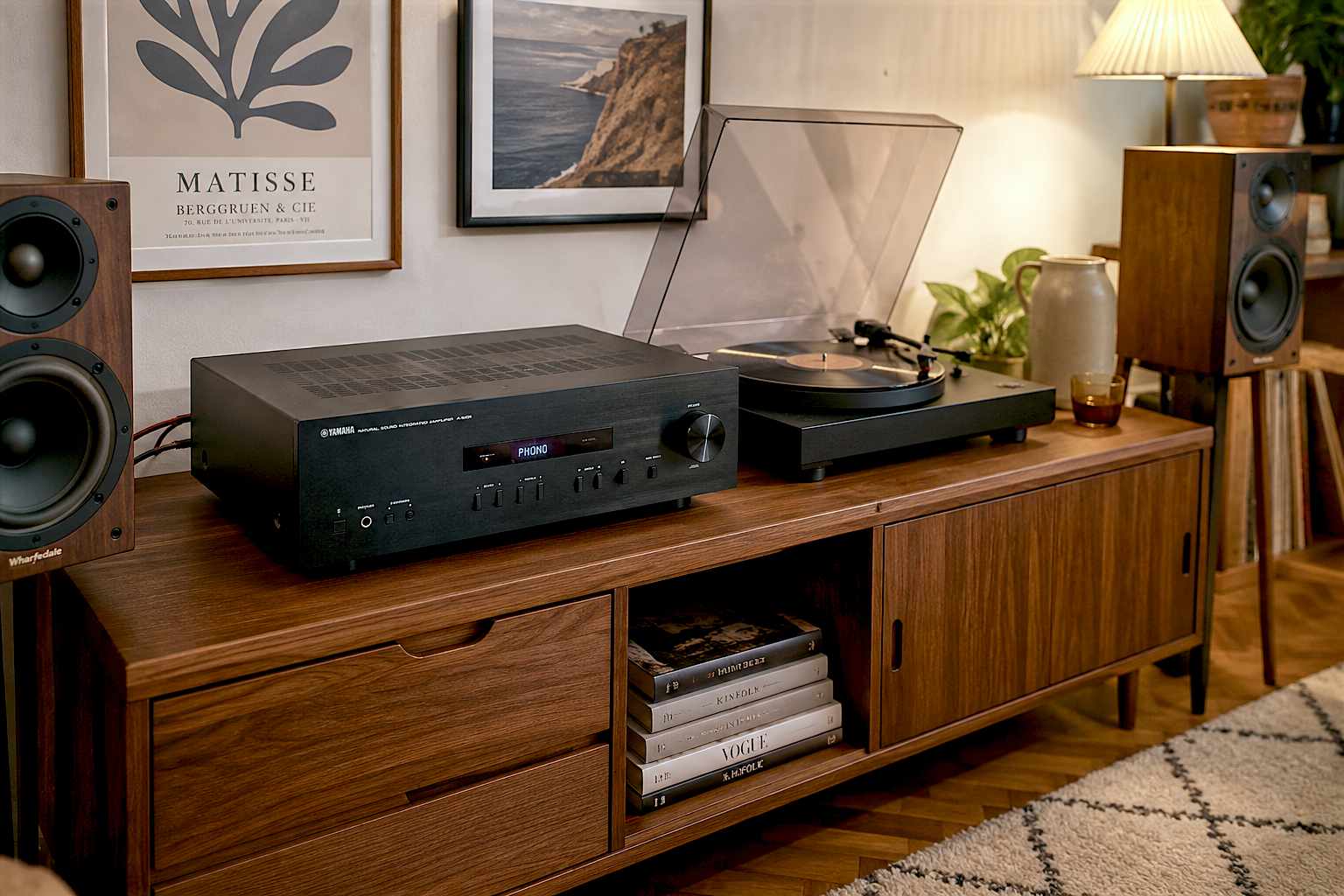A hyper-realistic, beautifully lit photograph of a black Yamaha A-S201 amplifier sitting on a mid-century modern wooden AV unit in a cozy UK living room. A vinyl record is playing on a sleek turntable next to it, and thick speaker wire runs to a pair of walnut bookshelf speakers. Warm, inviting lighting.