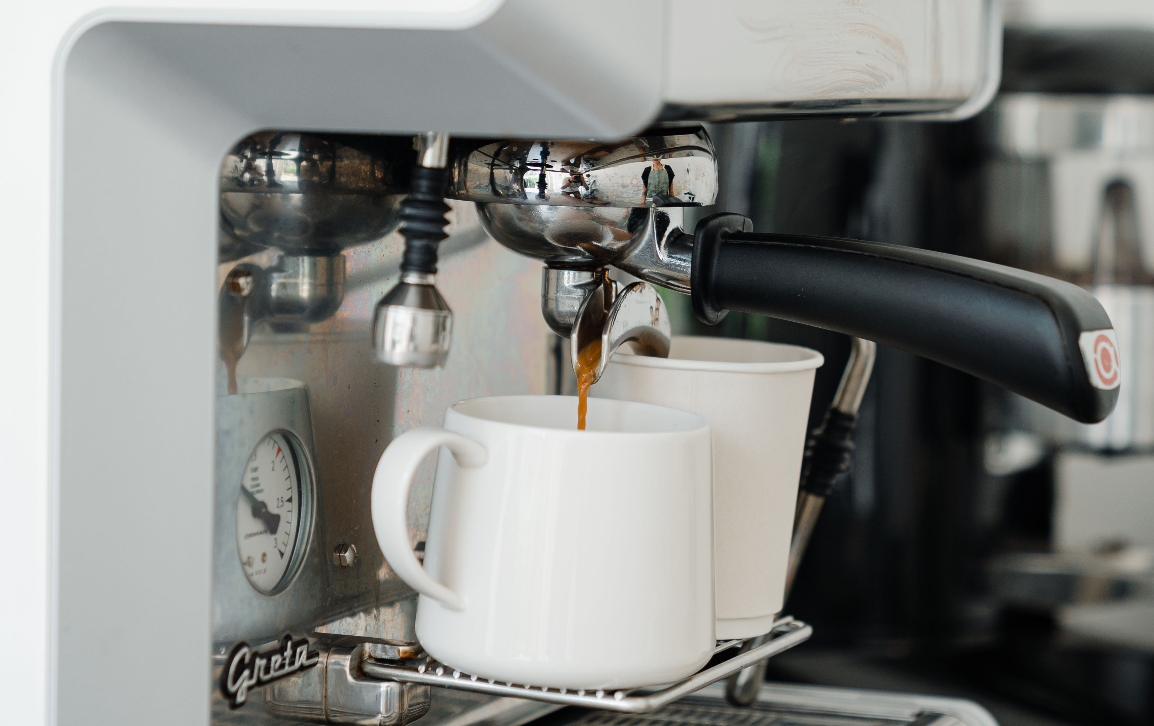 Coffee machine pouring fresh brewed aromatic coffee into ceramic mug and disposable cup